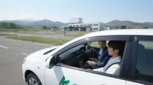 晴天の伊達自動車学校の所内コースを走行する普通教習車